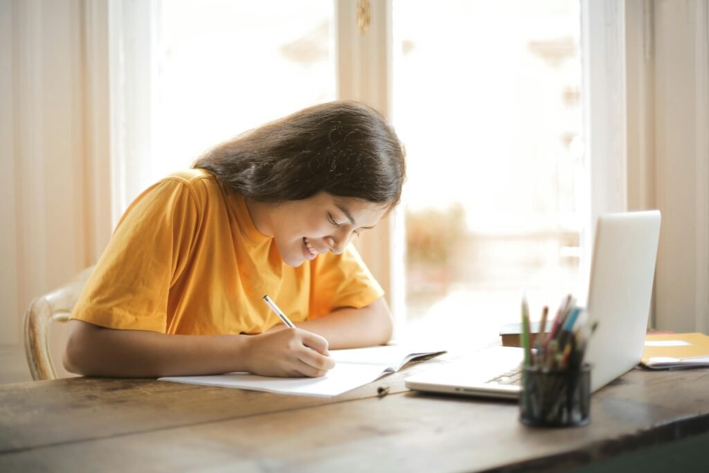Young woman studying with a laptop and notepad at home smiling and focused