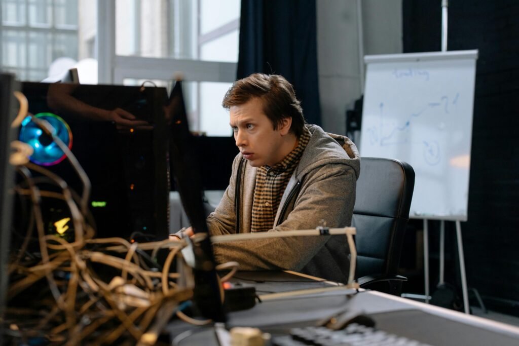 Young man intensely focused on computer work in a tech office setting with a whiteboard in the background.